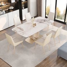 a dining room table with white chairs and a rug on the floor in front of it