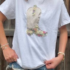 a woman standing in front of a wooden fence wearing a white shirt with a boot on it