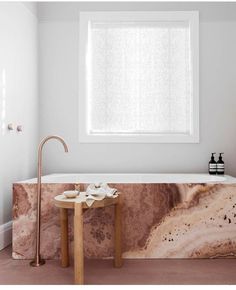 a marble bathtub in the middle of a bathroom with a wooden table next to it