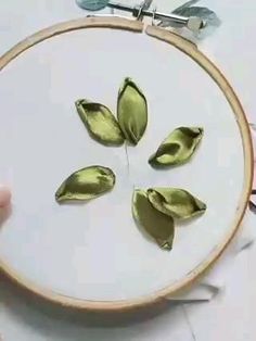 a person is holding a embroidery hoop with green leaves on it