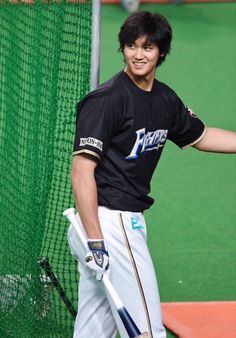 a young man holding a baseball bat next to a batting cage on a green field