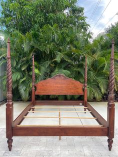 a wooden bed frame sitting on top of a stone floor in front of trees and bushes