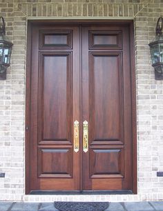 two brown double doors are on the side of a brick building with lanterns hanging above them