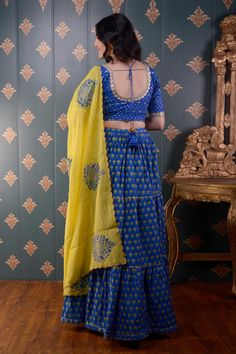 Royal blue tiered lehenga with floral block print motifs and gota patti trim on the hem. Comes with mirror embroidered blouse and lemon yellow floral print dupatta.
Component: 3
Pattern: Print and Embroidery
Type Of Work: Block Print and Mirror
Neckline: Round
Sleeve Type: Half
Fabric: Lehenga: Cotton Silk, Blouse: Banarasi Chanderi and Dupatta: Chanderi
Color: Blue
Other Details: 
Printed dupatta with scalloped border
Tie up with tassels on the side
Lace trim on the neckline and sleeve hems
Low Bollywood Style Choli With Zari Work And Tiered Skirt, Designer Traditional Tiered Lehenga, Festive Sharara With Dupatta And Tiered Skirt, Traditional Lehenga With Tiered Skirt For Festivals, Traditional Festival Lehenga With Tiered Skirt, Traditional Tiered Sharara For Festivals, Festive Lehenga With Tiered Skirt And Dupatta, Traditional Tiered Lehenga For Festivals, Festive Tiered Lehenga With Dupatta