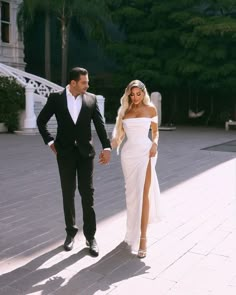 a man and woman dressed in formal wear walking down a sidewalk holding hands with each other