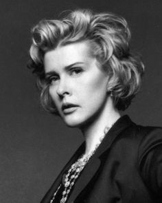 a black and white photo of a woman with short hair wearing a suit, necklace and pearls