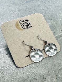 - Get ready to rock the quirky silver disc earrings! These small hammered discs have a 15mm diameter and a sweet 27mm drop. Made with stainless steel ear wires, they come on a branded card with clear ear backs. Unconventionally stylish and versatile, these hammered silver disc earrings will add a touch of cool to any outfit. With a 15mm diameter and 27mm drop, they're perfect for any occasion. Crafted with durable stainless steel ear wires, these earrings come on a branded card with clear ear backs for easy, breezy wear. So go ahead and add a bit of eccentricity to your earring game - your ears deserve the best! Indiana Love, Baby Jewelry, Disc Earrings, Garden Print, Bag Icon, Print Book, Easy Breezy, Hammered Silver, Corporate Gifts