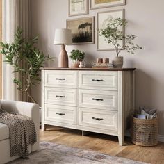 a white dresser sitting in a living room next to a window with pictures on the wall