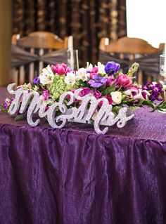 the table is covered with purple and white flowers, silver mr and mrs letters on it