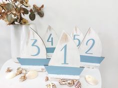 three wooden sailboats with numbers and seashells on a table