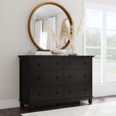 a black dresser with a round mirror above it and a white rug on the floor