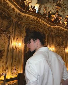 a man standing in front of a gold painted wall with lights on it's ceiling