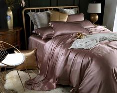 a bed with pink sheets and pillows in a room next to a chair, table and lamp