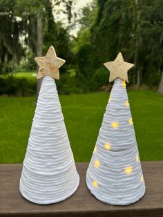 two white christmas trees with gold stars on them sitting on a wooden table in front of some grass