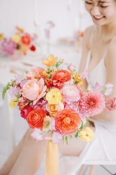 a woman sitting on a chair holding a bouquet of pink and yellow flowers in her hand