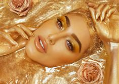 a woman laying on top of a bed covered in gold sheets and makeup looks at the camera