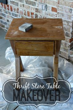 a wooden table sitting on top of a plastic bag next to a brick wall with the words thrift store table makeover