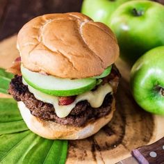 a hamburger sitting on top of a cutting board next to green apples