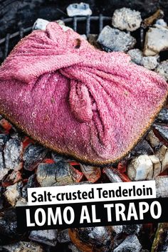 a pink bag sitting on top of a pile of rocks next to a grill with the words salt - crusted tenderion lomo al trapo