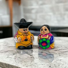 two ceramic figurines sitting on top of a marble counter