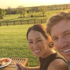 two women sitting at a picnic table in the grass and one is holding a fork