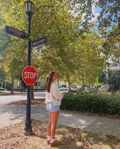 a woman standing under a stop sign next to a lamp post with street signs on it