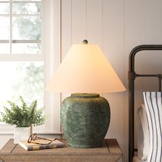 a green vase sitting on top of a wooden table next to a lamp and pillows