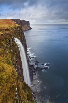 a large waterfall in the middle of a body of water next to a rocky cliff