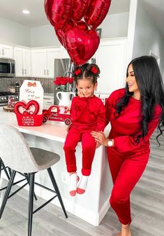 a mother and daughter in matching red outfits sitting on a kitchen counter with heart balloons