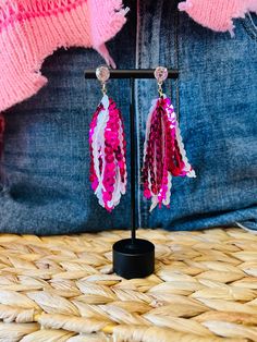 the pink and white beaded earrings are hanging from a black stand on a woven basket