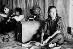 black and white photograph of people sitting on the floor with suitcases in front of them