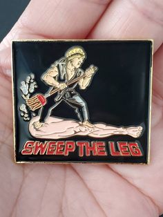 a hand holding a lapel pin with the words sweep the leg and an image of a man on it