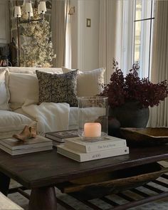 a coffee table with books and candles on it in front of a couch, window