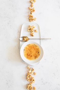 a white plate topped with popcorn next to a spoon and bowl filled with something brown