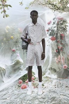 a man standing in front of a flower covered backdrop wearing white shoes and shorts with his hands on his hips