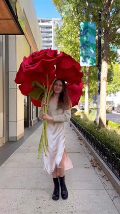 a woman is walking down the street with a large red rose in her hand and an umbrella over her head