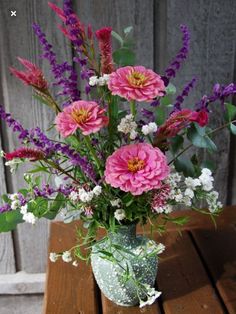 a vase filled with pink and purple flowers on top of a wooden table next to a fence