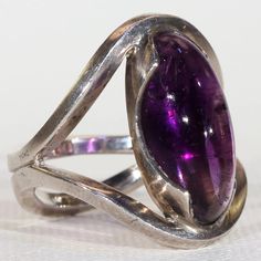 This Midcentury Modern ring is all about those clean lines and the rich color of the cabochon cut stone. It was designed by Otto Rasmussen and hand crafted in about 1950 of sterling silver. The ring is fairly large in scale and set with an amethyst of 9.51 carats which measures 20x9.1x7.3 mm, the stone shows some wonderful color banding and is more clear at the bottom than in the center. The stone is set in this striking silver mount that holds it securely at the top and bottom. This ring measur Luxury Formal Cabochon Amethyst Ring, Luxury Formal Amethyst Cabochon Ring, Luxury Amethyst Cabochon Ring For Formal Occasions, Elegant Formal Cabochon Ring, Fine Jewelry Silver Cabochons For Formal Occasions, Luxury Amethyst Cabochon Ring, Formal Cabochon Amethyst Ring Fine Jewelry, Silver Cabochons For Formal Fine Jewelry, Silver Cabochons For Formal Occasions