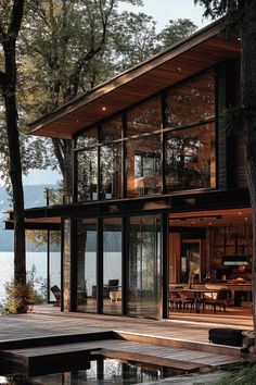 a house that is next to the water with trees in front of it and an open deck