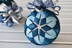 two blue ornaments with bows on them sitting on a white wooden table next to each other