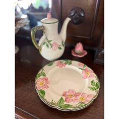 a tea pot and saucer with pink flowers on it sitting on a wooden table