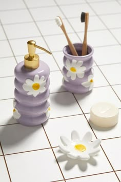 two toothbrush holders with flowers on them sitting on a tiled floor next to a white flower