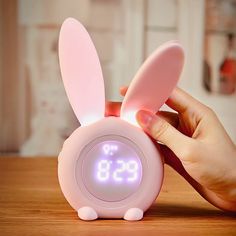 a pink alarm clock with bunny ears on it's face and hands holding the clock