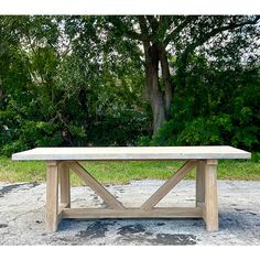 a wooden table sitting on top of a cement ground next to trees and grass in the background