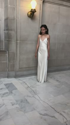 a woman in a white dress standing next to a wall with a light on it