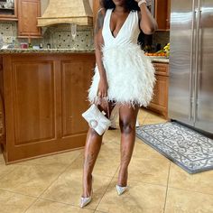 a woman standing in a kitchen wearing a white dress and holding a purse with her right hand