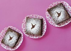 three pieces of cake sitting on top of pink paper plates covered in powdered sugar