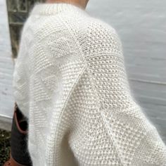 the back of a person's white sweater and brown booties standing in front of a body of water