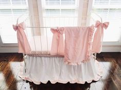 a crib with pink and white ruffled bedding in front of a window