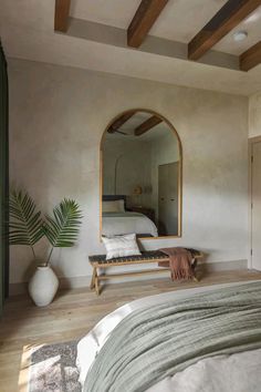 a bedroom with a bed, mirror and plant in it